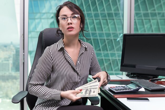 Joven empresaria posando en la oficina con dinero en efectivo