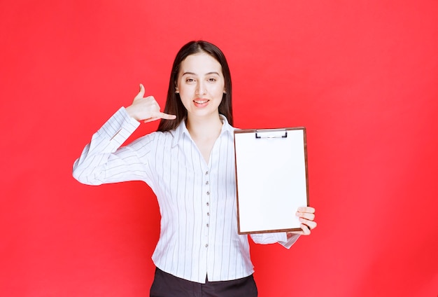 Joven empresaria positiva sosteniendo portapapeles vacío y posando.