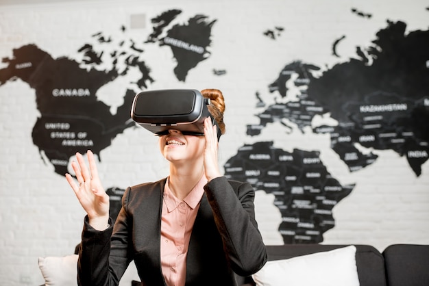 Foto joven empresaria probando gafas de realidad virtual sentados en el interior con mapa del mundo en el fondo