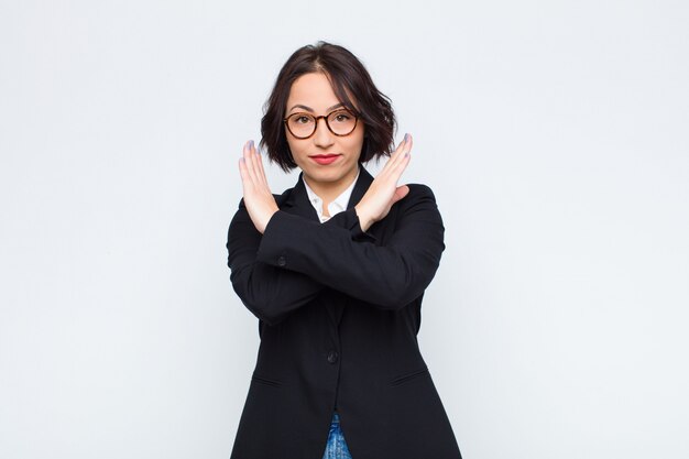 ¡Joven empresaria que parece molesta y harta de tu actitud, diciendo lo suficiente! las manos cruzadas al frente, diciéndote que te detengas sobre la pared blanca