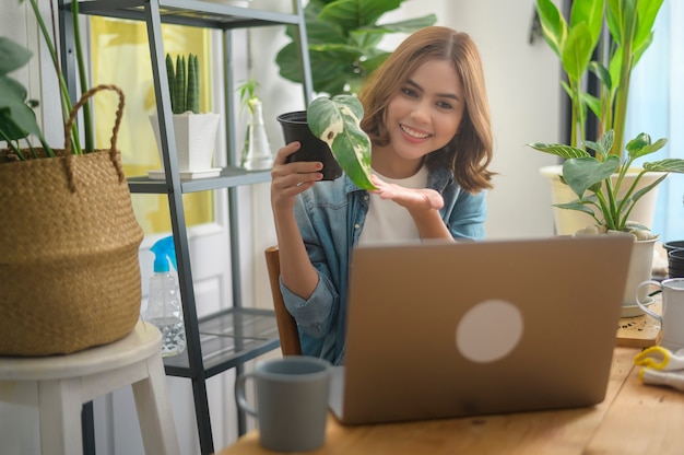 Una joven empresaria que trabaja con una computadora portátil presenta plantas de interior durante la transmisión en vivo en línea en casa