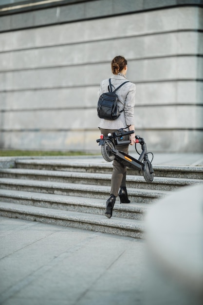 Una joven empresaria que va a trabajar con un scooter eléctrico.