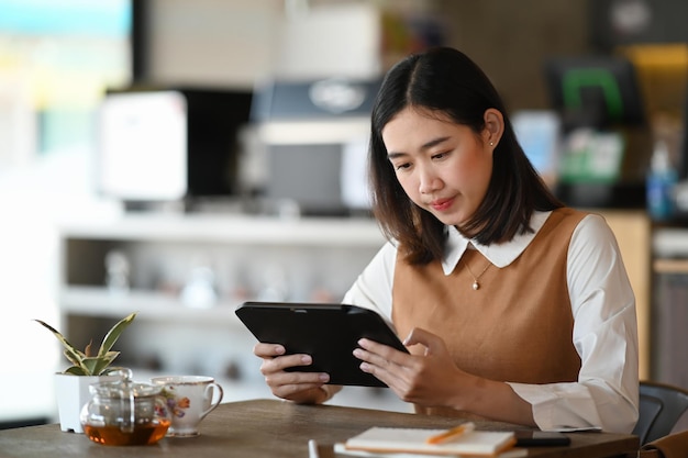 Joven empresaria relajándose en la cafetería y usando tableta digital.