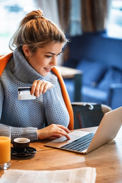 Joven empresaria relajándose en un descanso para tomar café y usando una tarjeta de crédito y una computadora portátil para comprar en línea