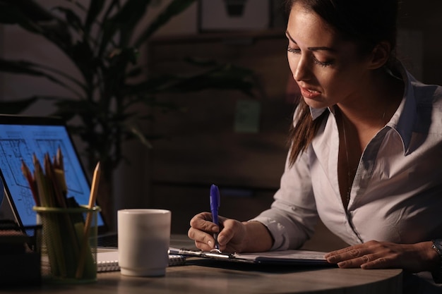 Joven empresaria revisando informes comerciales y escribiendo notas en el papel