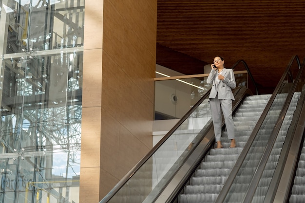 Joven empresaria en ropa formal de pie en las escaleras mecánicas dentro del gran centro comercial