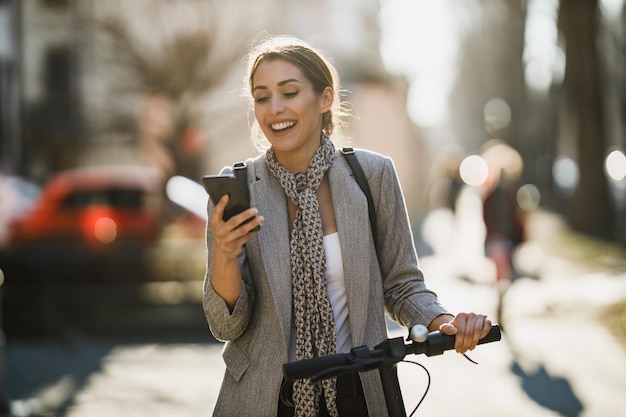 Una joven empresaria con un scooter eléctrico que va a trabajar y usa un teléfono inteligente.