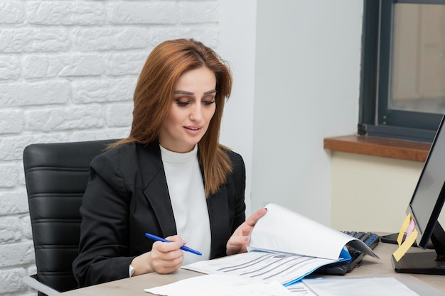 Joven empresaria sentada en el escritorio y escribiendo sus notas