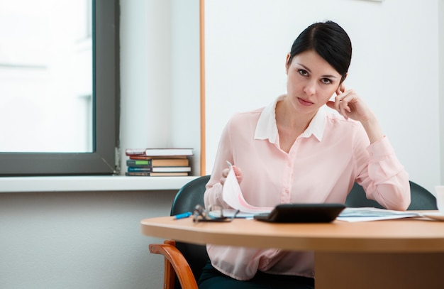 Joven empresaria sentada en el lugar de trabajo y leyendo el papel en la oficina