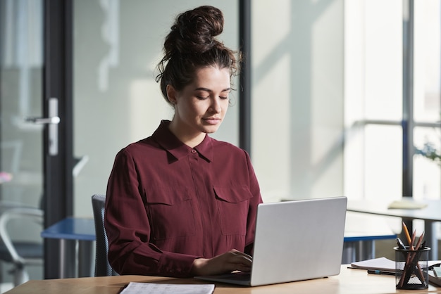 Joven empresaria sentada en su lugar de trabajo y trabajando en línea escribiendo en la computadora portátil en la oficina