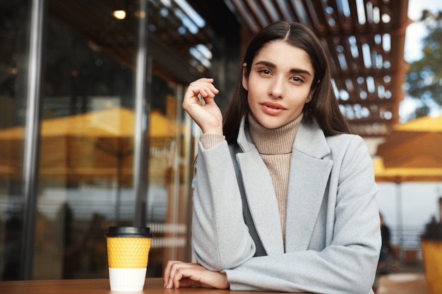 Joven empresaria sentado en el café al aire libre, mirando confiado en la cámara.