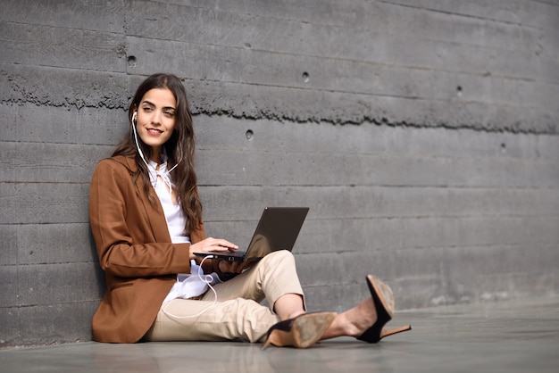 Joven empresaria sentado en el piso mirando su computadora portátil. Hermosa mujer llevaba desgaste formal con auriculares.