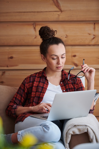 Foto joven empresaria seria mirando datos en línea en la pantalla del portátil mientras navega por la red en casa