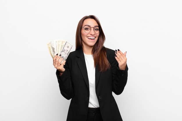 Joven empresaria sintiéndose feliz, sorprendida y alegre, sonriendo con actitud positiva, dándose cuenta de una solución o idea con billetes de dólar