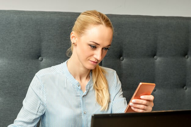 Joven empresaria con smartphone sentado en la mesa con un portátil en el café