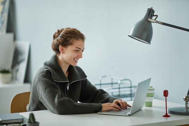 Joven empresaria sonriendo mientras se comunica en línea en una computadora portátil en su lugar de trabajo en la oficina