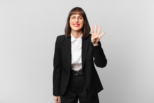 Joven empresaria sonriendo y mirando amistosamente, mostrando el número cuatro o cuarto con la mano hacia adelante, contando hacia atrás