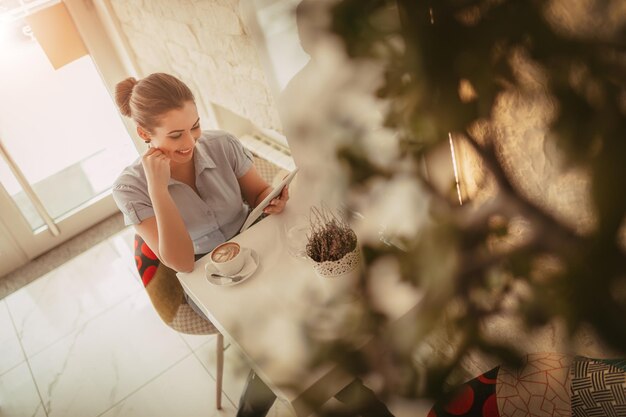 Foto joven empresaria sonriente en un descanso en un café. ella está usando una tableta digital y bebe café.