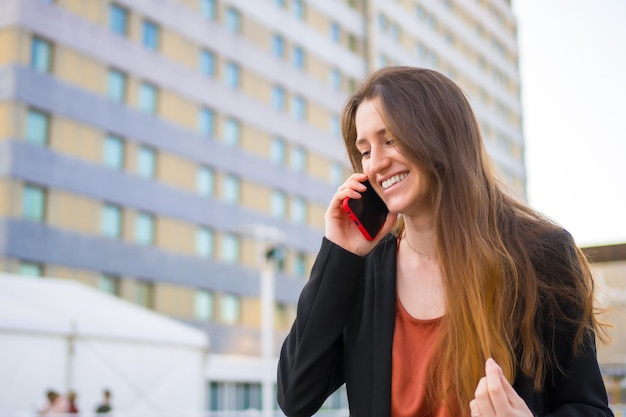 Una joven empresaria sonriente hablando con el móvil junto a los edificios de la ciudad