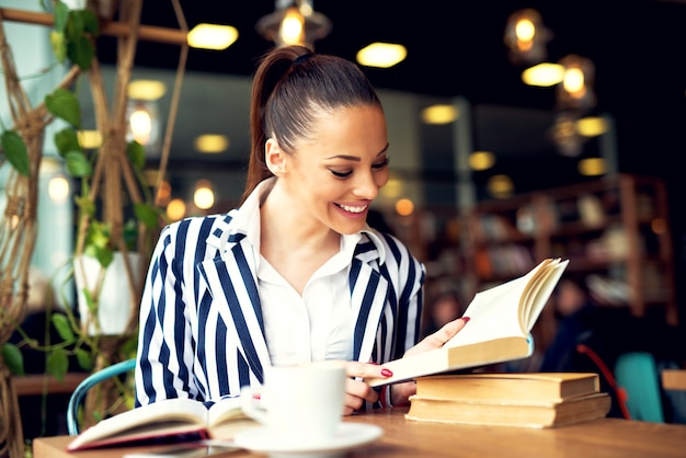 Joven empresaria sonriente sentado a la mesa en la cafetería y libro de lectura.