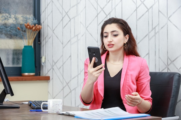 Joven empresaria sosteniendo su teléfono y mirándolo Foto de alta calidad