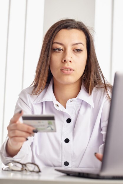 Joven empresaria sosteniendo una tarjeta de crédito y mirando la computadora portátil.