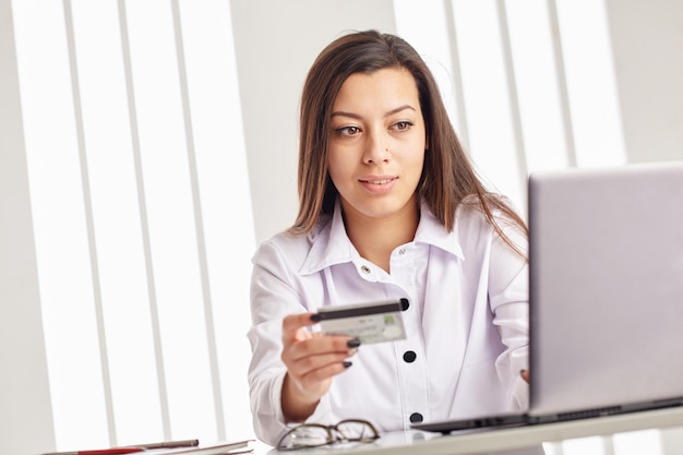 Joven empresaria sosteniendo una tarjeta de crédito y mirando la computadora portátil.