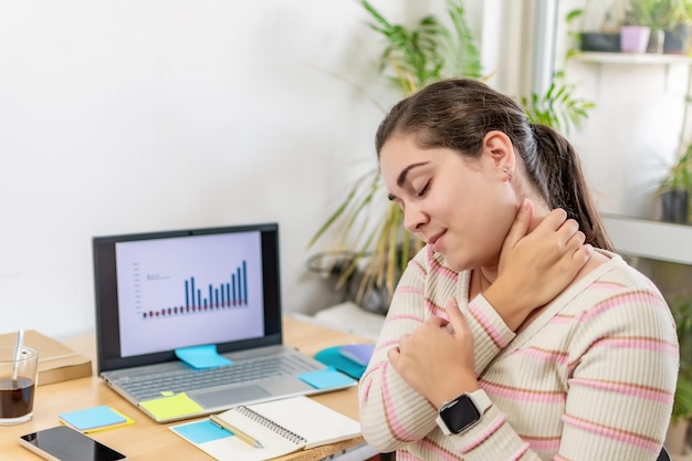 Joven empresaria tocando el cuello rígido de masaje después del trabajo sedentario en la computadora