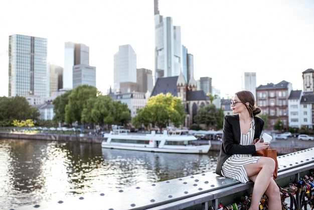Joven empresaria tomando un café al aire libre sentado en el puente en la ciudad de Frankfurt