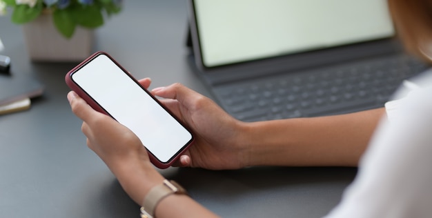 Joven empresaria trabajando en su proyecto mientras usa el teléfono inteligente en el lugar de trabajo moderno