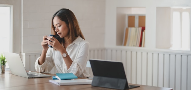 Joven empresaria trabajando en su proyecto y tomando una taza de café en la oficina moderna