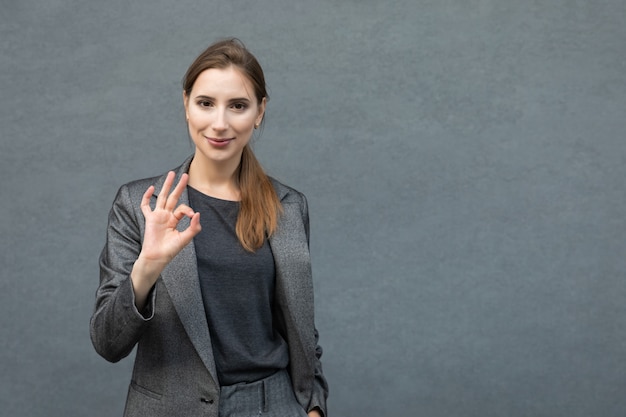 Una joven empresaria en un traje gris con gesto OK