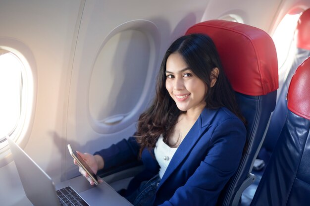 Una joven empresaria vestida con traje azul está usando una computadora portátil a bordo