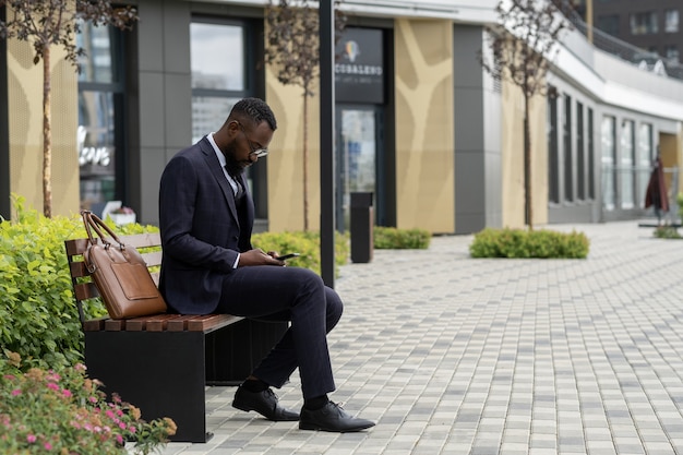 Joven empresario africano barbudo desplazándose en smartphone