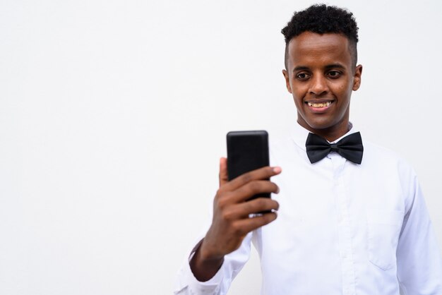 Joven empresario africano guapo mediante teléfono móvil contra el fondo blanco.