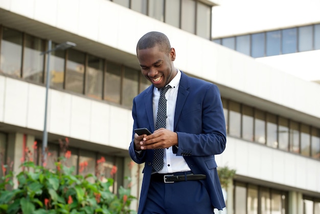 Joven empresario africano sonriente caminando con un teléfono inteligente en la ciudad