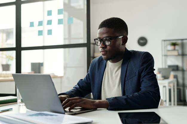 Joven empresario afroamericano serio con laptop trabajando en escritorio