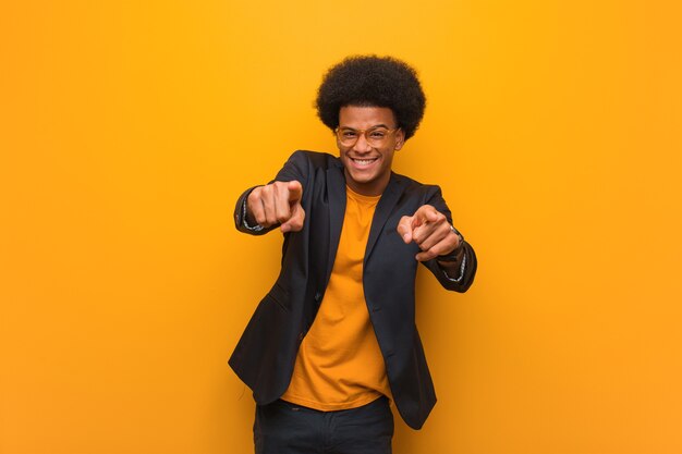 Joven empresario afroamericano sobre una pared naranja alegre y sonriente apuntando hacia el frente