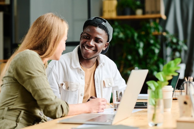 Joven empresario afroamericano sonriente escuchando a una colega