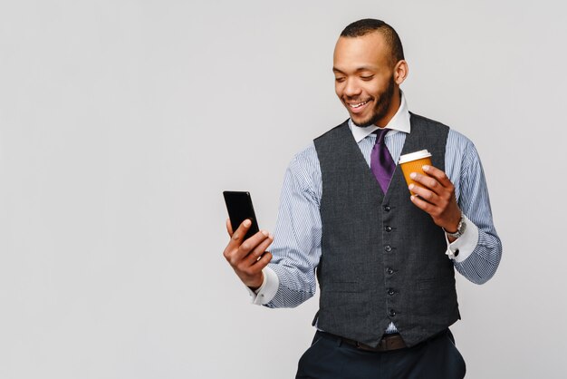 Joven empresario afroamericano con teléfono y café para ir gris claro.