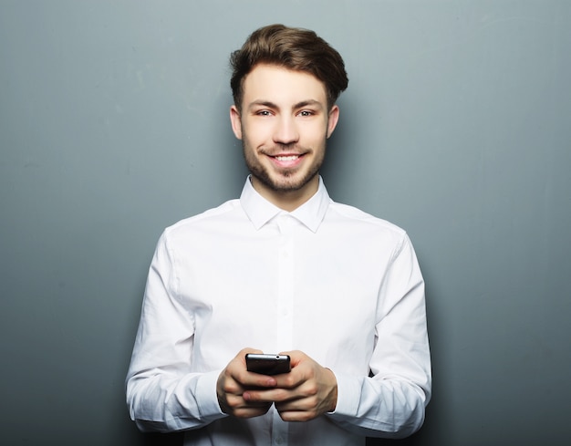 Joven empresario alegre escribiendo sms en su teléfono móvil