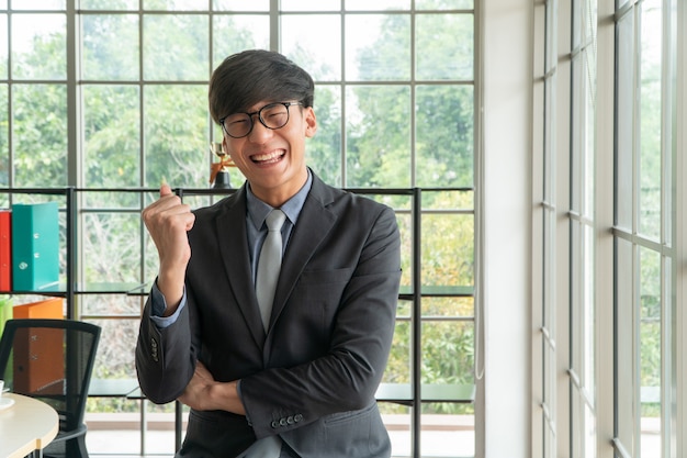 Joven empresario asiático emocionado feliz y celebrando el éxito en el lugar de trabajo