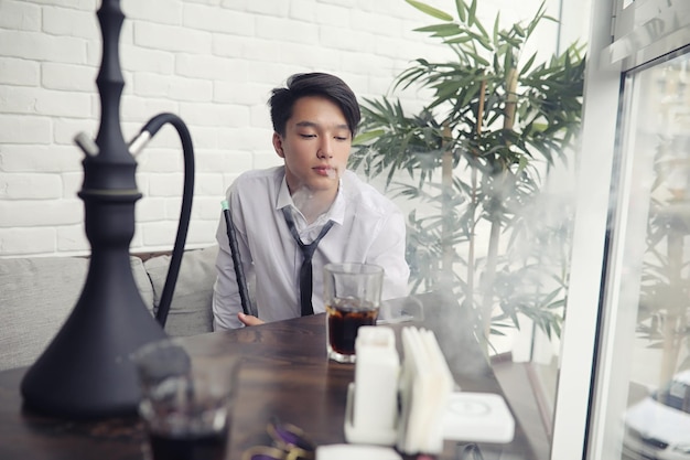Foto un joven empresario asiático está esperando a un socio en un café. reunión de negocios en el restaurante. un joven coreano hablando por teléfono en un café.