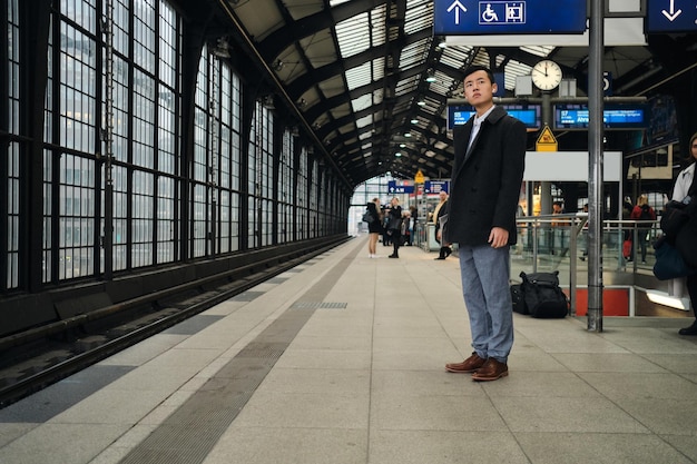 Joven empresario asiático con estilo esperando atentamente el tren en la estación de metro de la ciudad