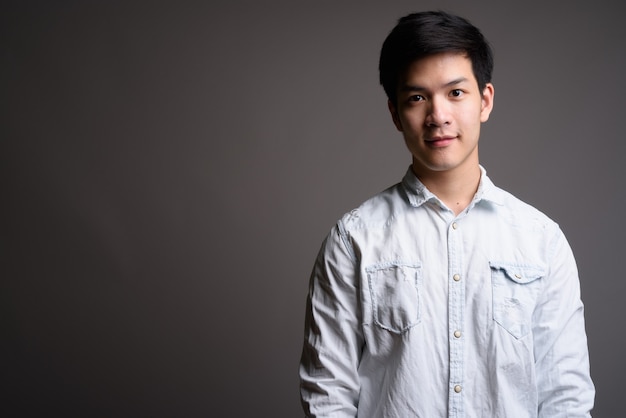 Joven empresario asiático guapo vistiendo camisa blanca sobre gris