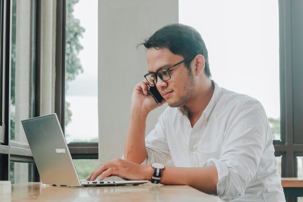 Joven empresario asiático hablando por un teléfono inteligente en un escritorio en el café