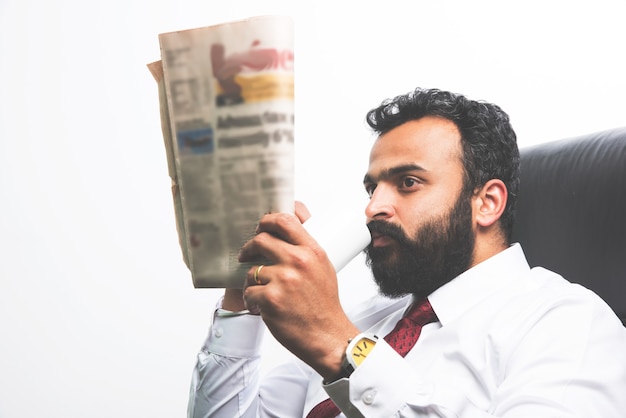 Joven empresario asiático indio leyendo el periódico mientras toma un café en la oficina