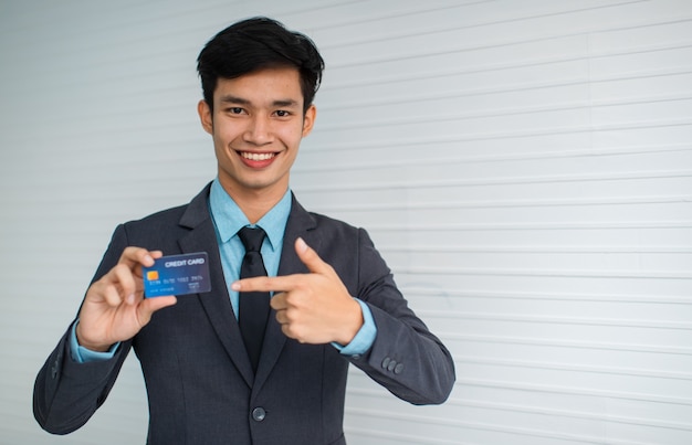 Joven empresario asiático sonriendo para cámara apuntando a la publicidad de tarjetas de crédito contra el servicio bancario