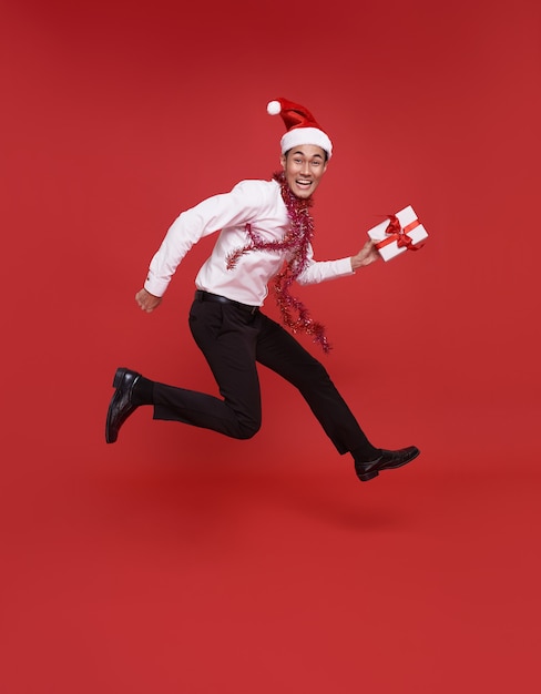 Joven empresario asiático vistiendo gorro de Papá Noel y sosteniendo una caja de regalo en la fiesta de Navidad