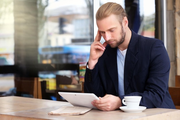 Joven empresario atractivo almorzando y trabajando en un café